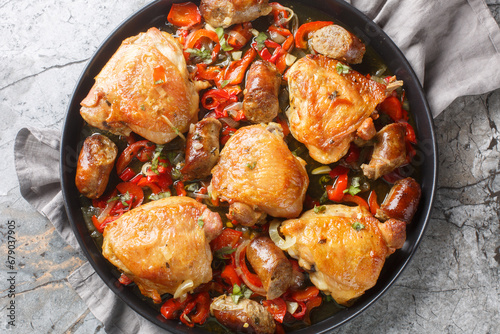 Braised chicken thighs, peppers and sausage in a vinegary, kind of spicy broth closeup on the plate on the table. Horizontal top view from above photo