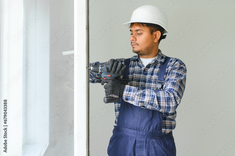 Indian Workman in overalls installing or adjusting plastic windows in the living room at home Indian Workman in overalls installing or adjusting plastic windows in the living room at home