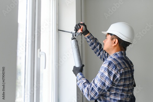 Indian worker using a silicone tube for repairing of window indoor photo