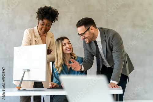 Group of happy multiethnic business people in formal wear gathered around computer in office