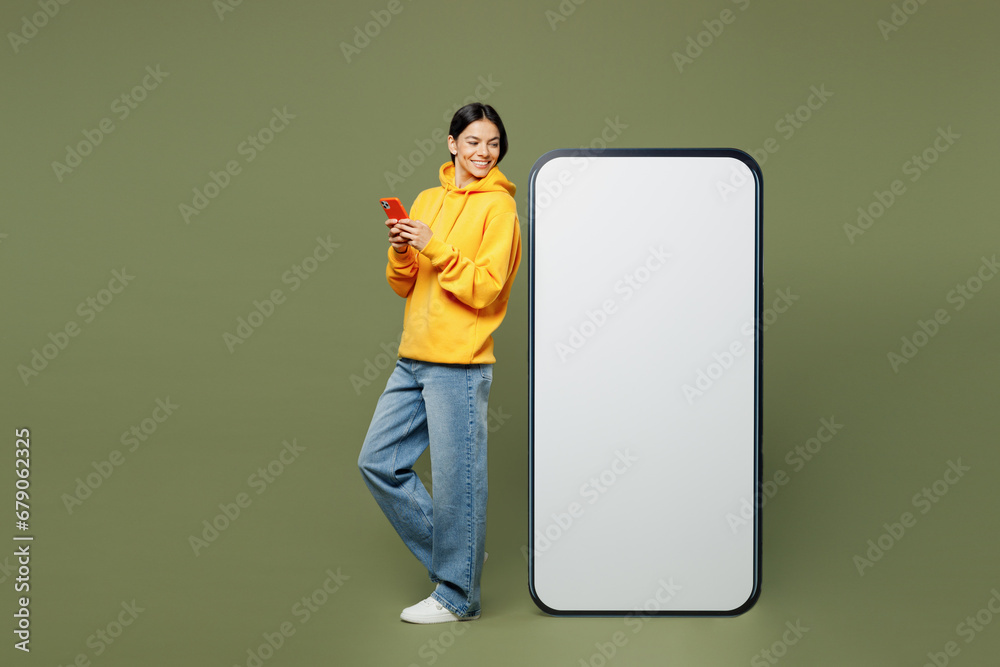 Φωτογραφία Full body young Latin woman she wearing yellow hoody casual clothes look at big huge blank screen mobile cell phone with area use smartphone isolated on plain pastel green background studio portrait