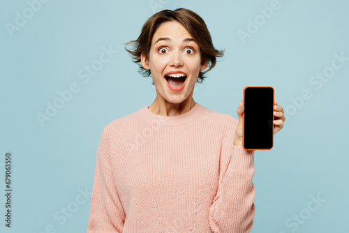 Young surprised woman wear beige knitted sweater casual clothes hold in hand use blank screen mobile cell phone chatting online isolated on plain pastel light blue cyan background. Lifestyle concept. photo
