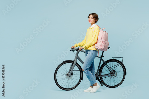 Full body young minded dreamful happy woman student wear casual clothes sweater backpack bag ride bicycle look aside on area isolated on plain blue background. High school university college concept.