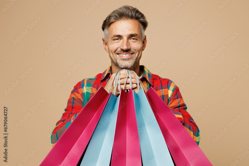 Young happy fun cool man wears casual clothes red shirt hold in hand paper package bags after shopping isolated on plain light pastel beige color background studio. Black Friday sale buy day concept.