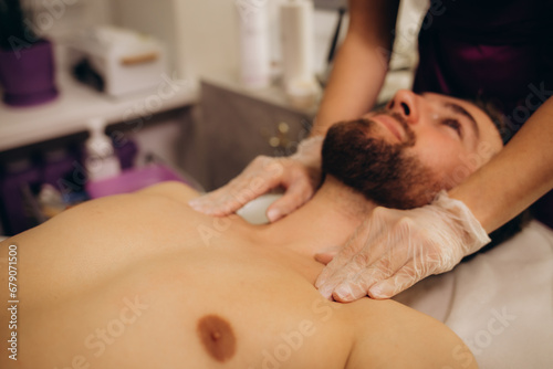 Masseur giving neck massage to young wealthy caucasian athlete in dark room of spa salon
