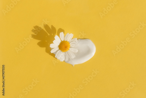 The texture of the cream with a chamomile flower on a yellow background. Smear of skincare cosmetics product. The concept of natural cosmetics. Top view