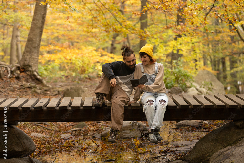 Fototapeta premium male and female couple reading an ebook in the forest with sitting on a bridge