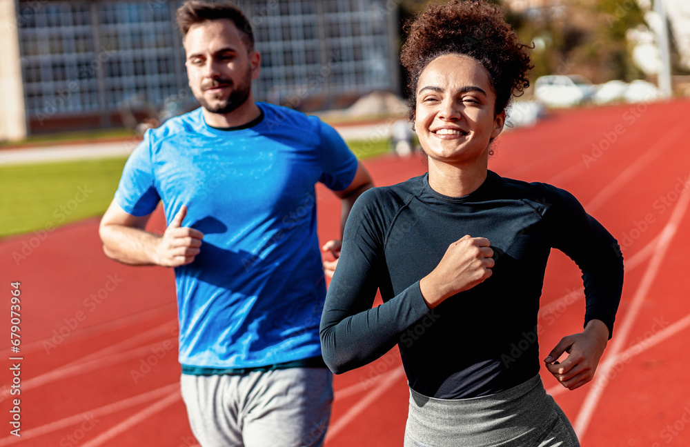Woman and man doing morning workout outdoors running on track.