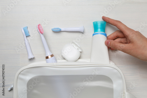 Electric toothbrushes, dental floss, tube in cosmetic bag and hand on white wooden background, top view