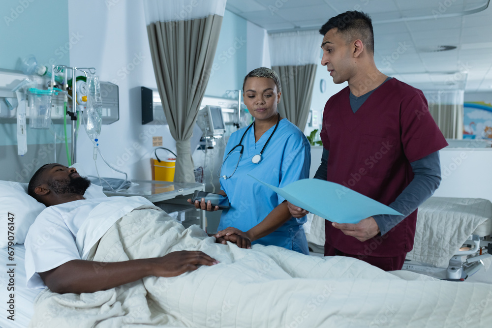 Diverse doctors and male patient is lying in bed talking in hospital room Diverse doctors and male patient is lying in bed talking in hospital room