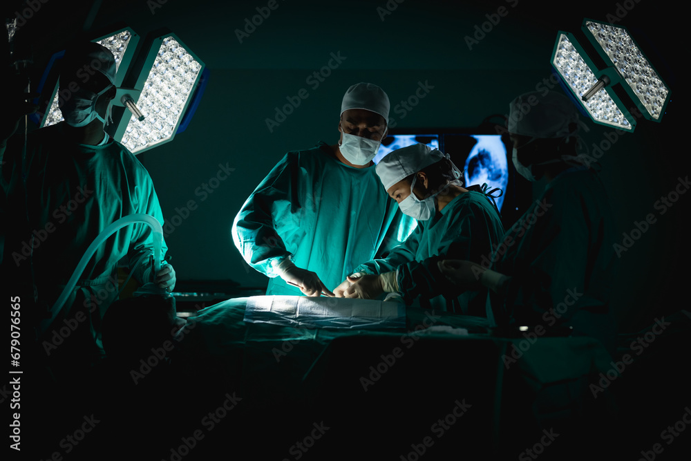 Diverse surgeons wearing surgical gowns operating on patient in operating theatre at hospital Diverse surgeons wearing surgical gowns operating on patient in operating theatre at hospital
