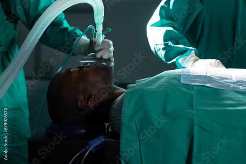 Diverse surgeons wearing surgical gowns using anaesthetic mask in operating theatre at hospital photo