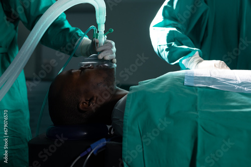 Diverse surgeons wearing surgical gowns using anaesthetic mask in operating theatre at hospital