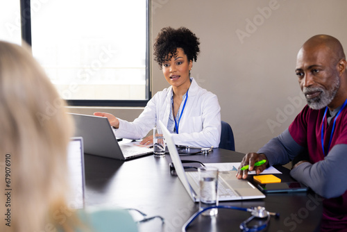 Happy diverse male and female medical staff with laptops talking at office meeting photo