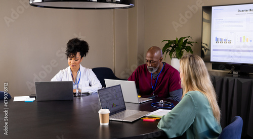 Diverse male and female medical staff with laptops working at office meeting photo