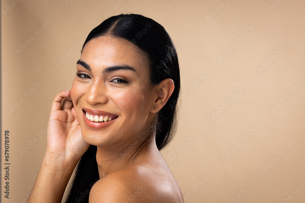 Smiling biracial woman with dark hair, hand to face, natural make up on brown background Smiling biracial woman with dark hair, hand to face, natural make up on brown background
