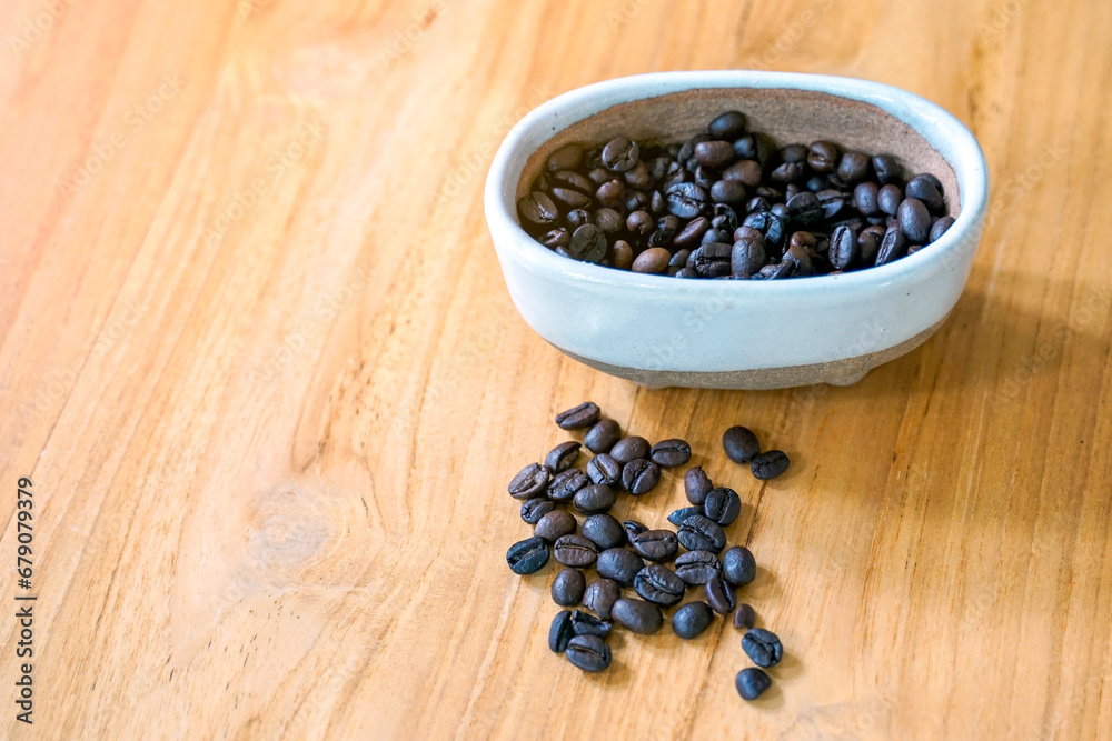 Coffee beans roasted in a ceramic bowl and spread on wooden table background. suitable for both hot and cold coffee. Soft and selective focus. Coffee beans roasted in a ceramic bowl and spread on wooden table background. suitable for both hot and cold coffee. Soft and selective focus.