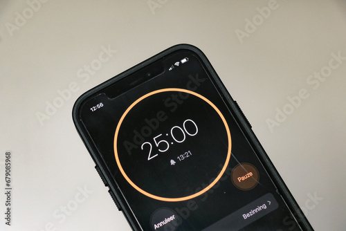 A phone with a black and orange 25-minute timer to study with the pomodoro method on a white blurry background