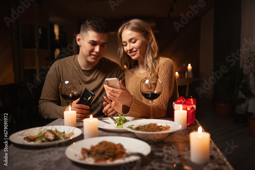 Happy young couple in love looking photos on smartphone during romantic dating or celebrating valentine s day at home