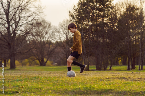 Sports training. Teenage boy of 11-13 years old in sports uniform trains on field with soccer ball in summer morning .
