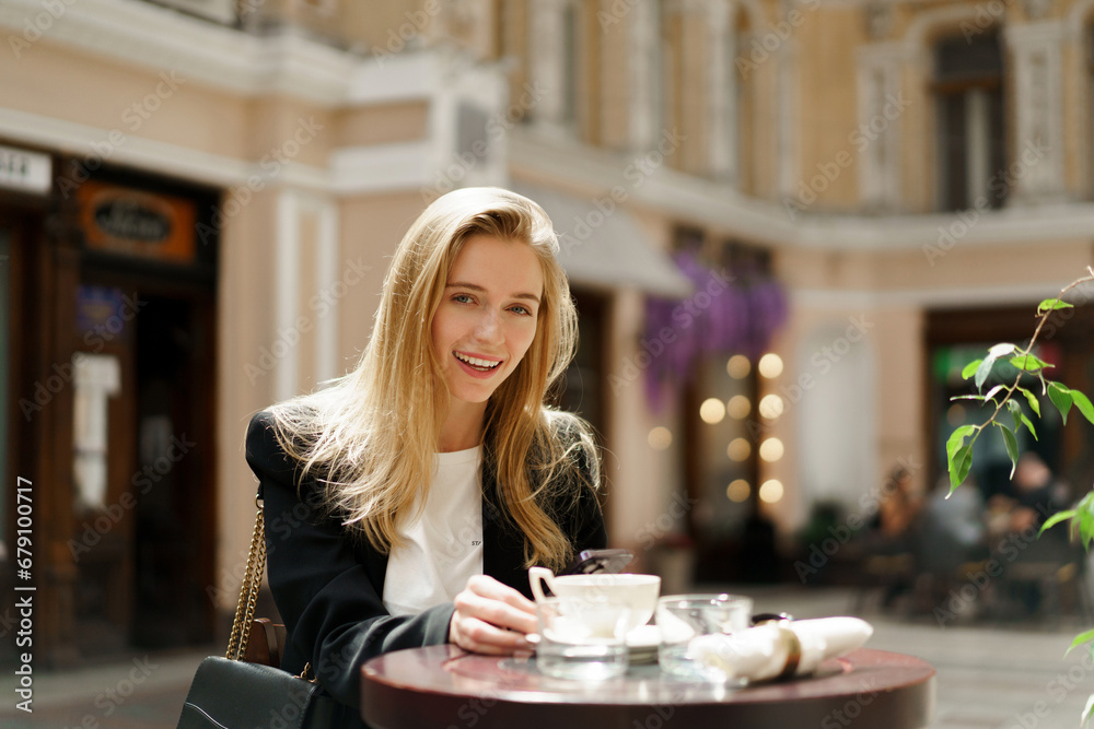 Beautiful blond woman in stylish casual business outfit sitting in cafe in beautiful european city. Enjoing coffee. Beautiful blond woman in stylish casual business outfit sitting in cafe in beautiful european city. Enjoing coffee.