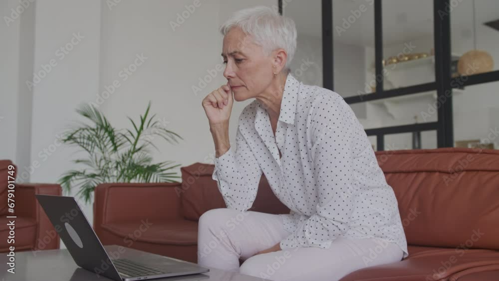 Pensive Mature Woman Reading on Laptop Indoors Pensive Mature Woman Reading on Laptop Indoors