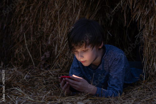 Fotografia Boy lies in haystack on summer night and reads something exciting from phone screen