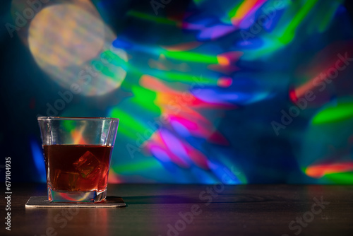 Glass of whiskey on the bar in front of the blur image Christmas background. Festive abstract background with bokeh defocused lights and stars