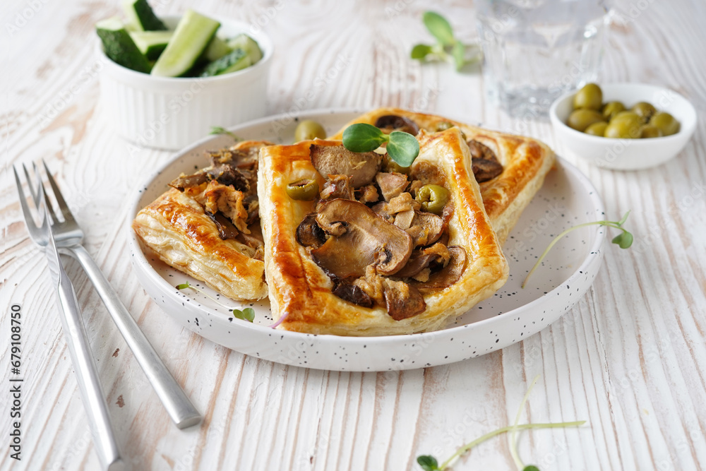 pastry with mushroom and olive filling on puff pastry, white ceramic plate, side bowl with olives, light wooden background, close-up pastry with mushroom and olive filling on puff pastry, white ceramic plate, side bowl with olives, light wooden background, close-up