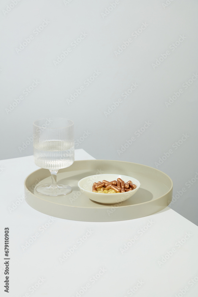 The pills are displayed on a white ceramic plate. A glass of water is placed on a round ceramic dish on a white table. Space for medicine advertising. The pills are displayed on a white ceramic plate. A glass of water is placed on a round ceramic dish on a white table. Space for medicine advertising.