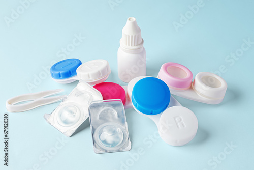 Contact lenses and pile of cases with eye drops bottle on blue background