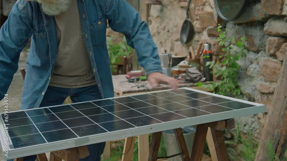 Medium long shot of senior man fixing broken solar power equipment at worktable outdoors Medium long shot of senior man fixing broken solar power equipment at worktable outdoors