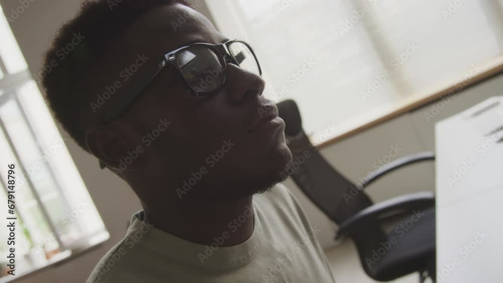 Handheld tilting up shot of young African American male programmer typing on keyboard and looking at computer monitor while developing software in open space minimalist office