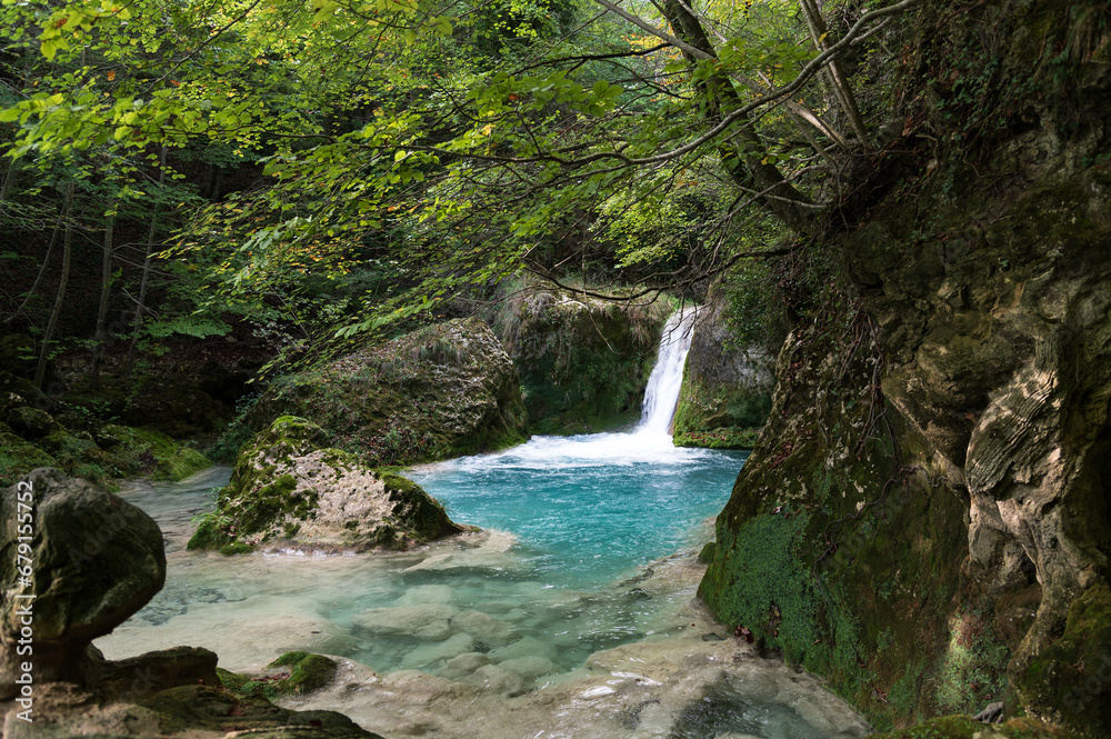 Vista de una cascada en el nacedero del río Urederra en la sierra de Urbasa con hayas y el agua del río, Navarra, España. Vista de una cascada en el nacedero del río Urederra en la sierra de Urbasa con hayas y el agua del río, Navarra, España.