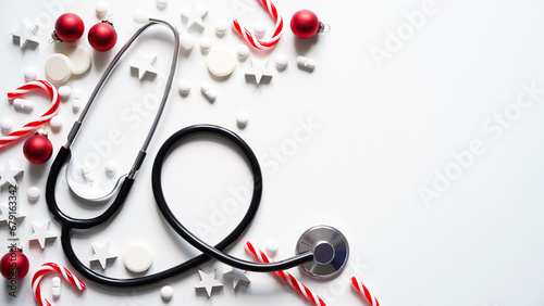 Christmas medical banner. Close-up of stethoscope, striped lollipops, red balls, stars and pills on white background, top view, flat lay, copy space. New Year's medicine, congratulations to doctor. photo