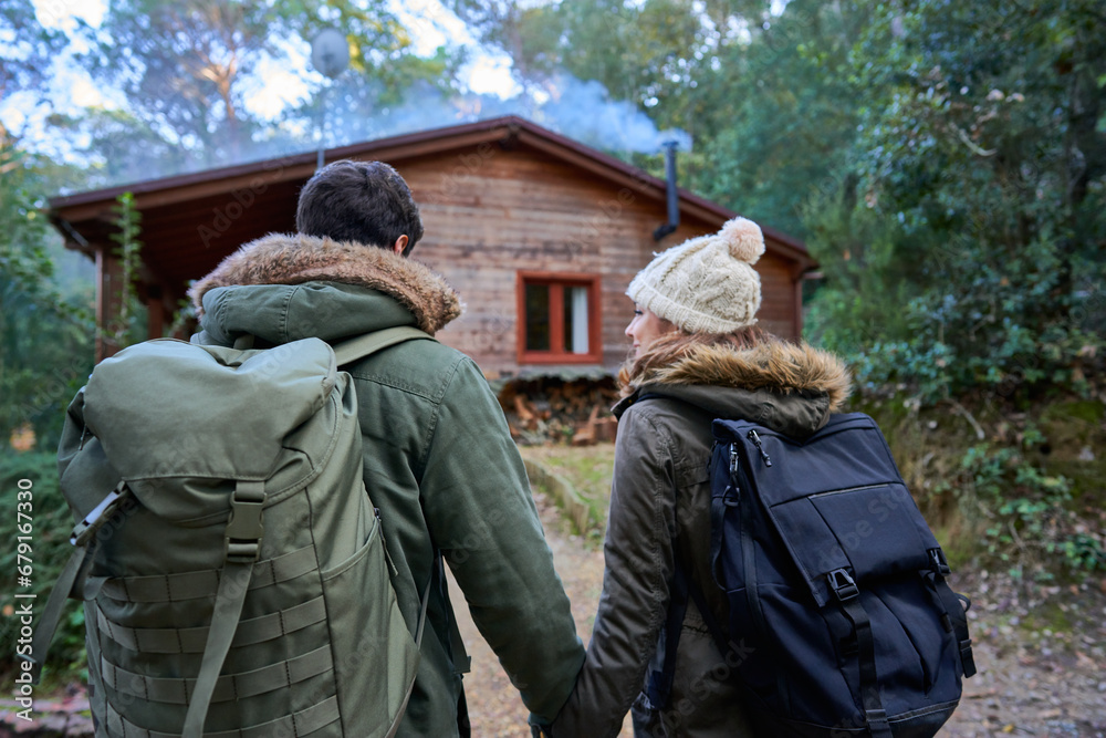 Couple with backpacks walk towards country house.