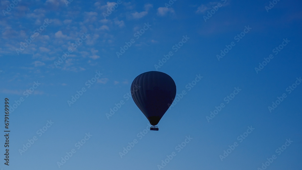 A hot air balloon with people floats in the dark sky, just before dawn. A hot air balloon with people floats in the dark sky, just before dawn.
