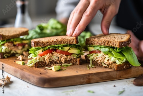 individual filling their sandwich with lettuce and tuna salad