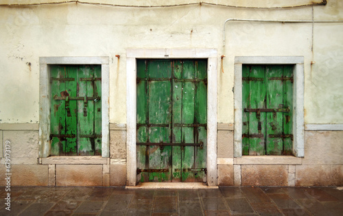 Shabby wall with windows and a green wooden door in Italy on the island of Chioggia