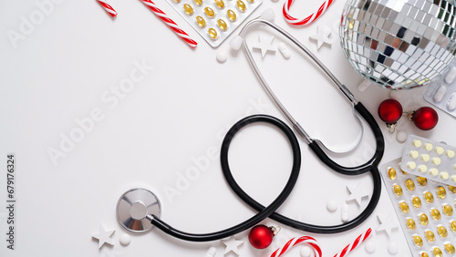 Christmas medical banner.Close-up of stethoscope,disco ball,striped lollipops,red balls,stars and pills on white background,top view,flat lay,copy space.New Year's medicine, congratulations to doctor.