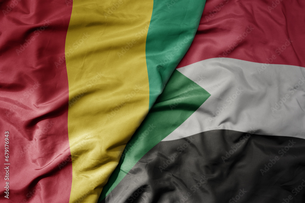 big waving national colorful flag of guinea and national flag of sudan .