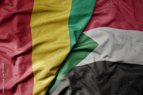 big waving national colorful flag of guinea and national flag of sudan .