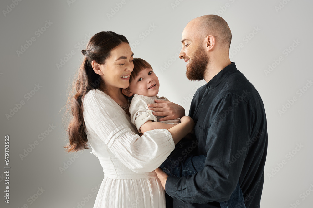 cheerful mother in white dress hugging her little son while her husband looking at them, family cheerful mother in white dress hugging her little son while her husband looking at them, family