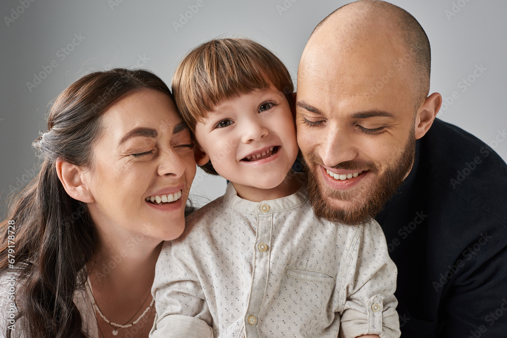 joyous loving parents smiling with closed eyes hugging their joyful little son, family concept joyous loving parents smiling with closed eyes hugging their joyful little son, family concept