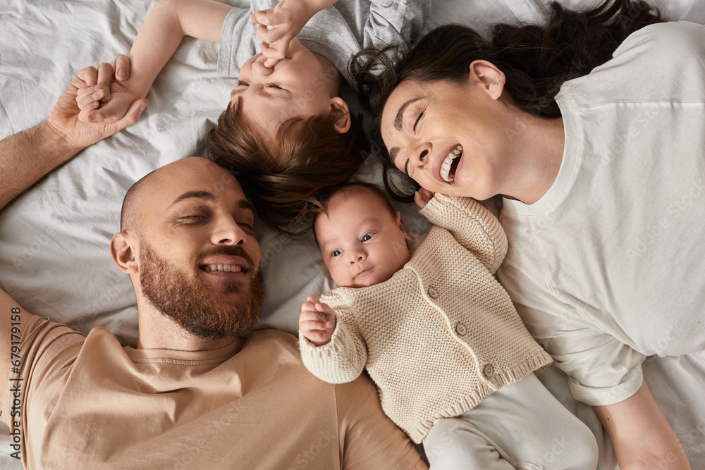 top view of joyous young modern family in cozy homewear lying on bed together and smiling happily