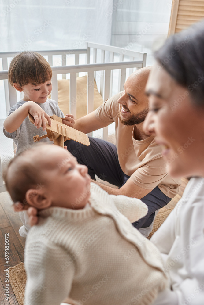vertical focused shot of happy father playing with his little son next to his blurred wife and baby vertical focused shot of happy father playing with his little son next to his blurred wife and baby