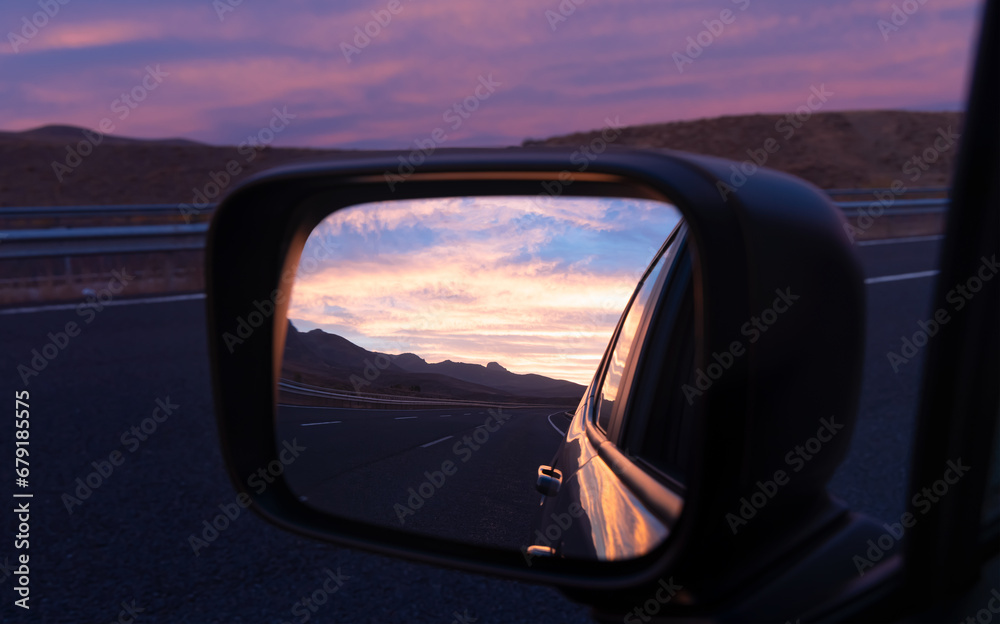 Sunrise or sunset from the left rearview mirror of a car driving on the highway ​