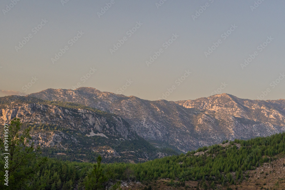 The last rays of the sun illuminate the mountains with sparse shrubs on them. - obrazy, fototapety, plakaty 