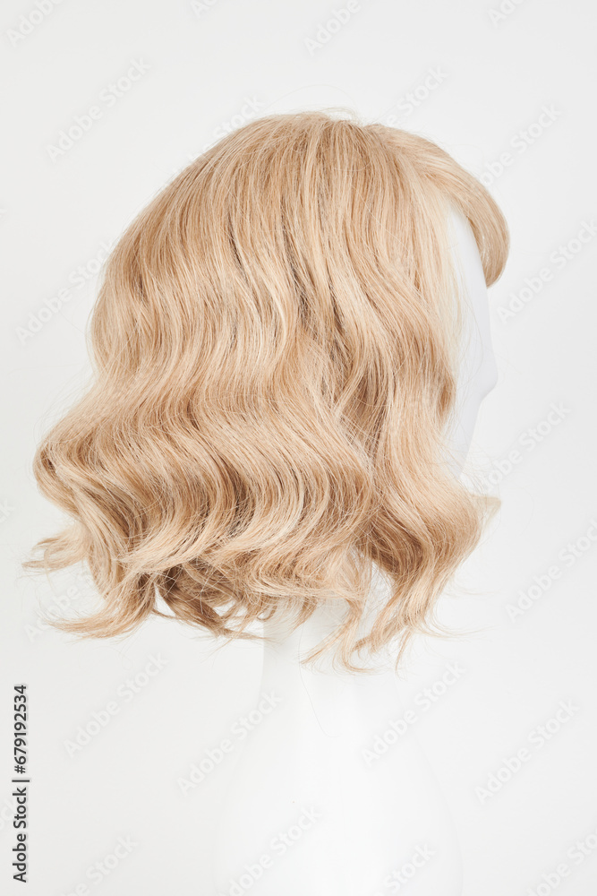 Naklejka premium Natural looking blonde fair wig on white mannequin head. Middle length hair cut on the plastic wig holder isolated on white background, side view.