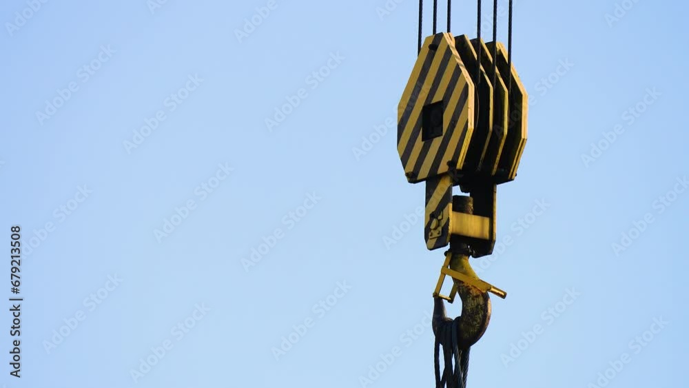 Close-up crane hook with steel cables, featuring construction paint finish, steel tool of labor against blue sky. Left side Copy space for placing text. Parts of construction crane, hook and slings Close-up crane hook with steel cables, featuring construction paint finish, steel tool of labor against blue sky. Left side Copy space for placing text. Parts of construction crane, hook and slings